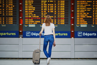 young woman in international airport with luggage and passport near flight information displ young woman in international airport with luggage and passport near flight information displ