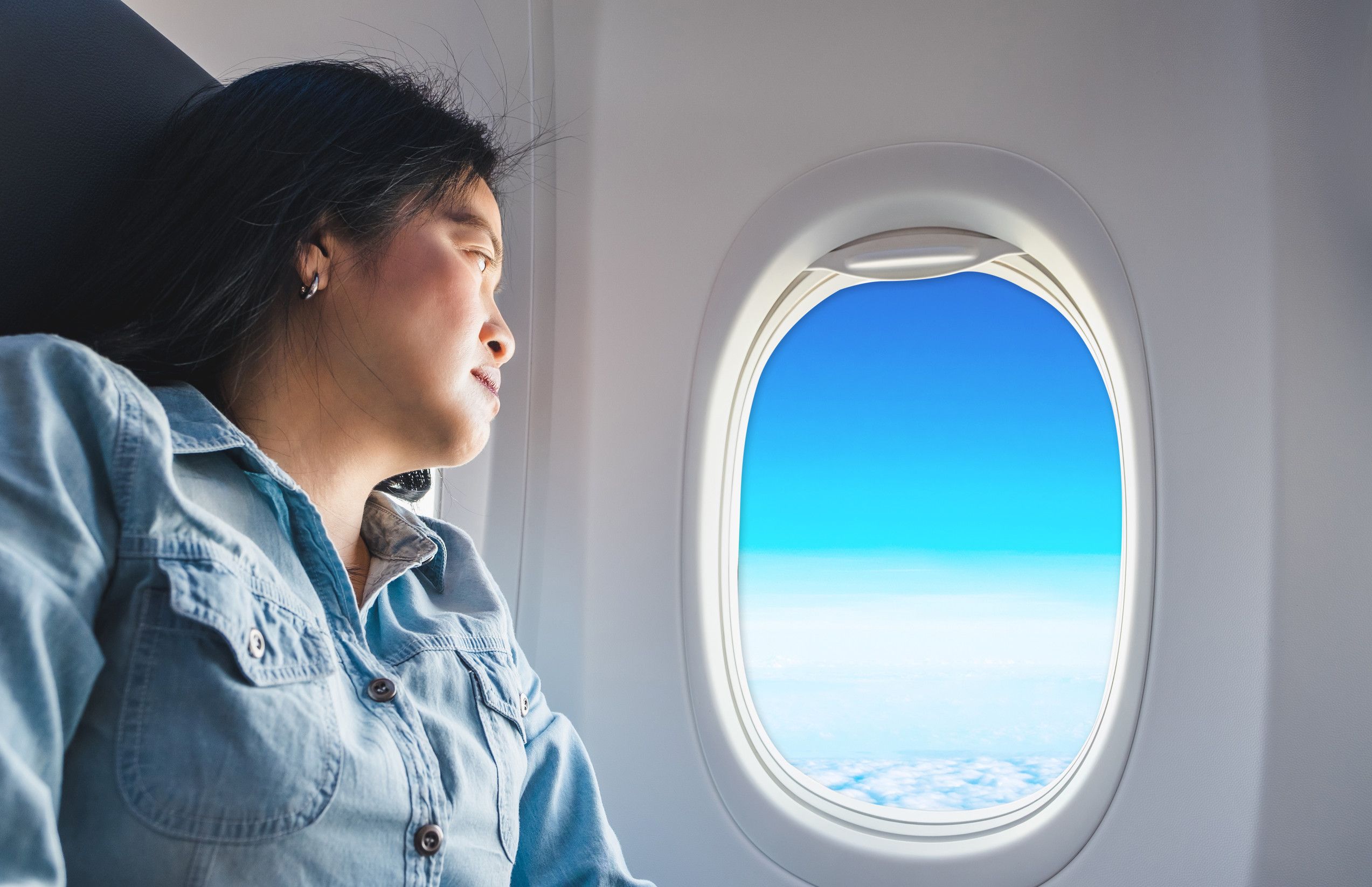 Une femme asiatique assise au hublot d'un avion regarde par la fenêtre et découvre le ciel bleu. Une femme asiatique assise au hublot d'un avion regarde par la fenêtre et découvre le ciel bleu.