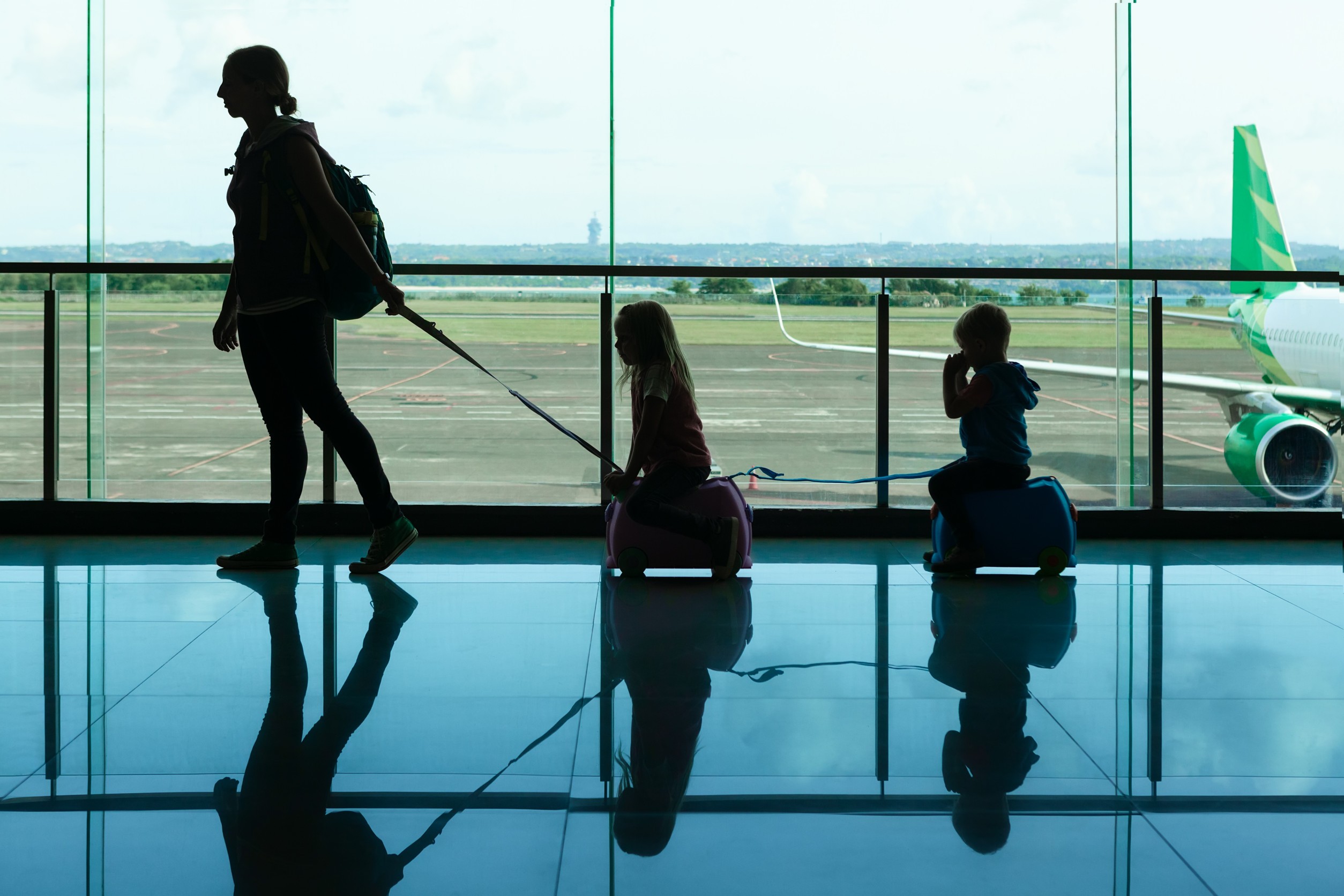Dans le hall de transit de l'aéroport, une jeune mère transporte des valises avec ses petits enfants jusqu'à la porte d'embarquement. Dans le hall de transit de l'aéroport, une jeune mère transporte des valises avec ses petits enfants jusqu'à la porte d'embarquement.
