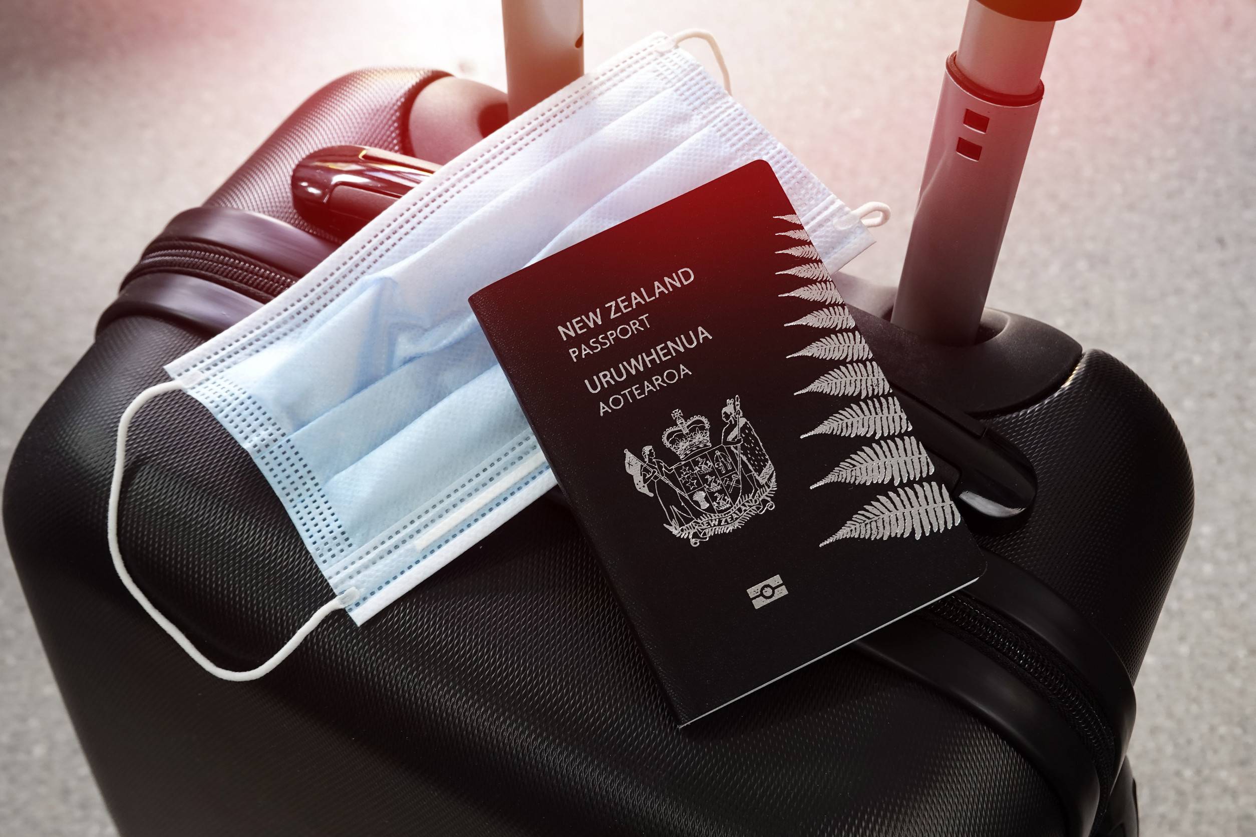 Passeport néo-zélandais et masque de protection sur une valise noire pendant la pandémie. Passeport néo-zélandais et masque de protection sur une valise noire pendant la pandémie.